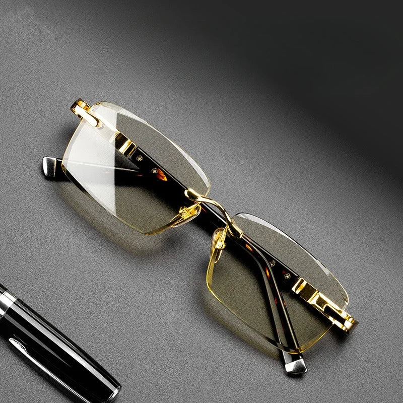 Rimless reading glasses with gold details and a pen on gray surface